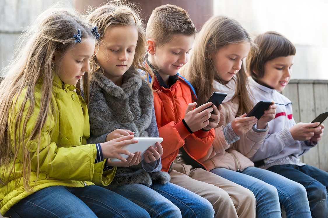 Ordinary kids sitting with mobile devices in street